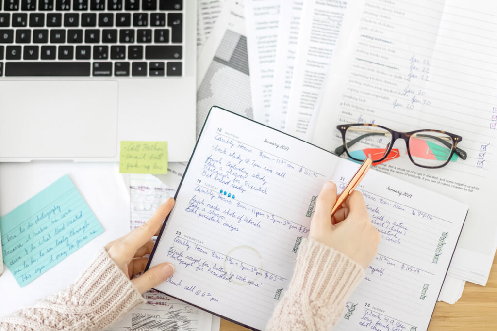 Woman Writing In a Planner on a Busy Desk